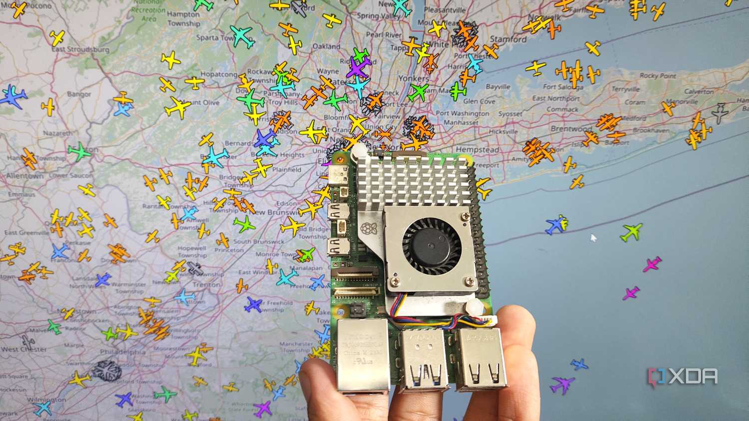 A person holding a Raspberry Pi 5 in front of an airplane tracking system