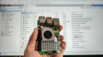 A person holding a Raspberry Pi in front of a PC