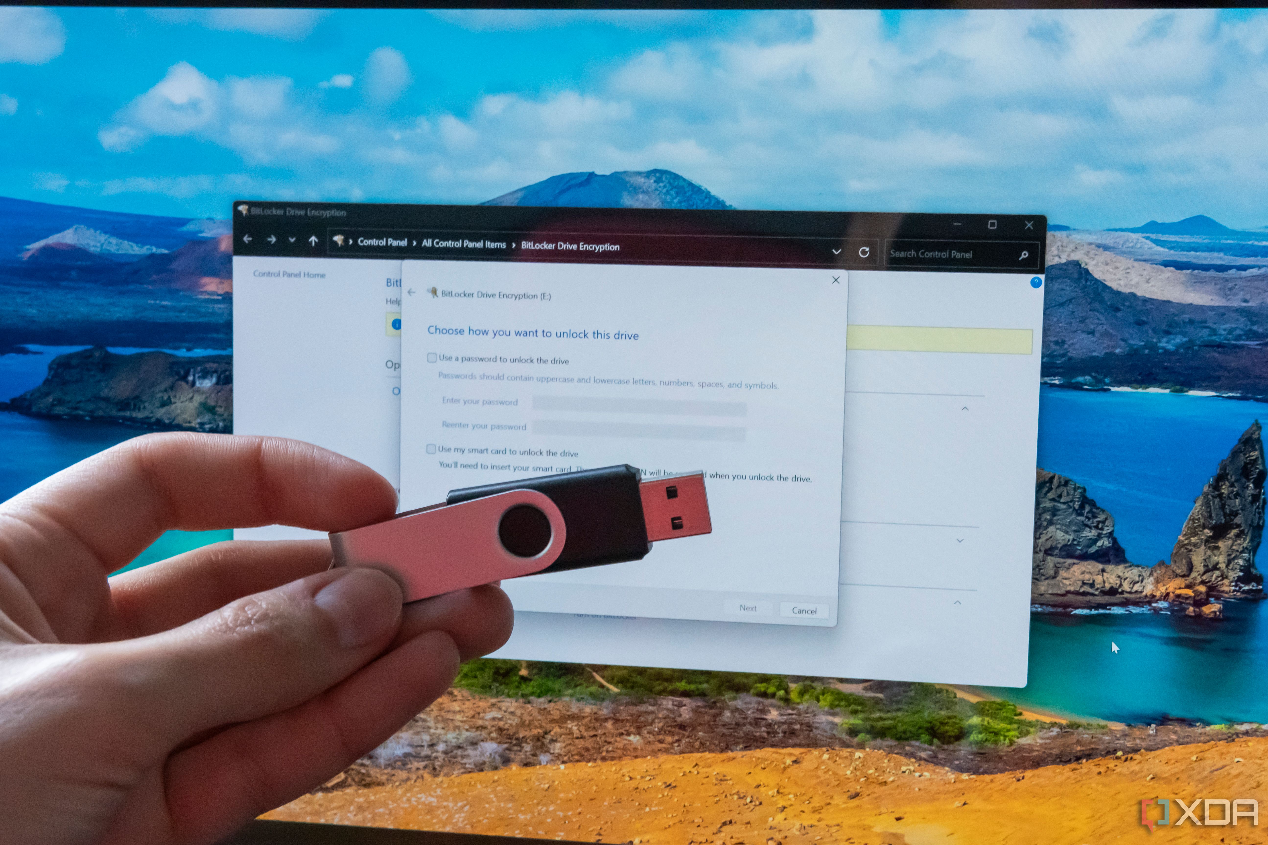 Hand holding a USB flash drive in front of a computer screen displaying BitLocker settings
