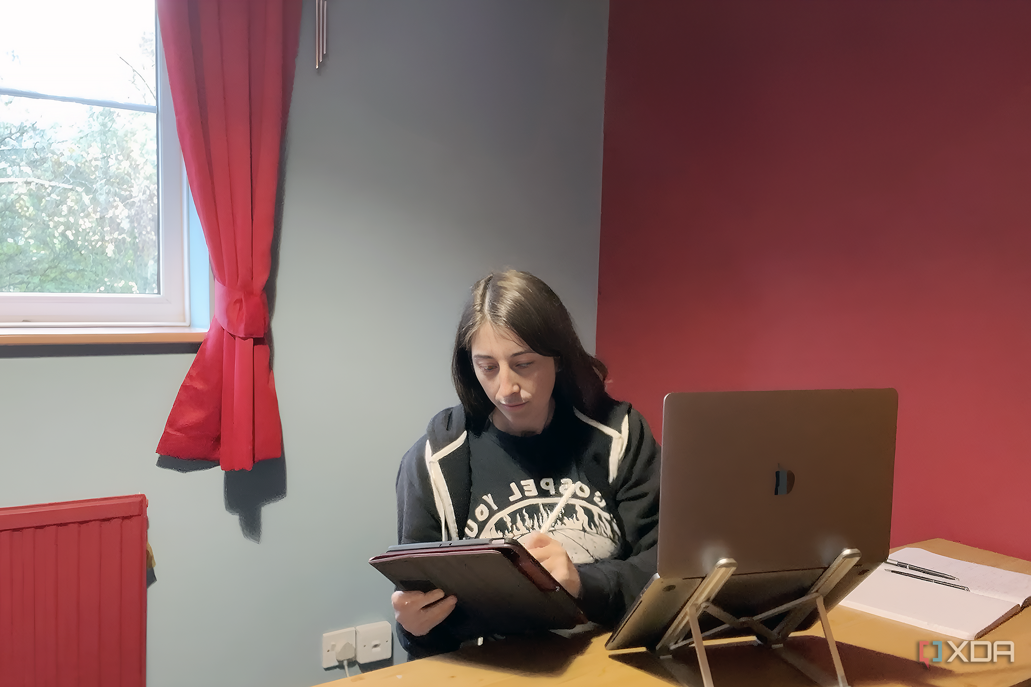 Woman at a work desk using an iPad and Apple Pencil next to a MacBook and a paper notebook