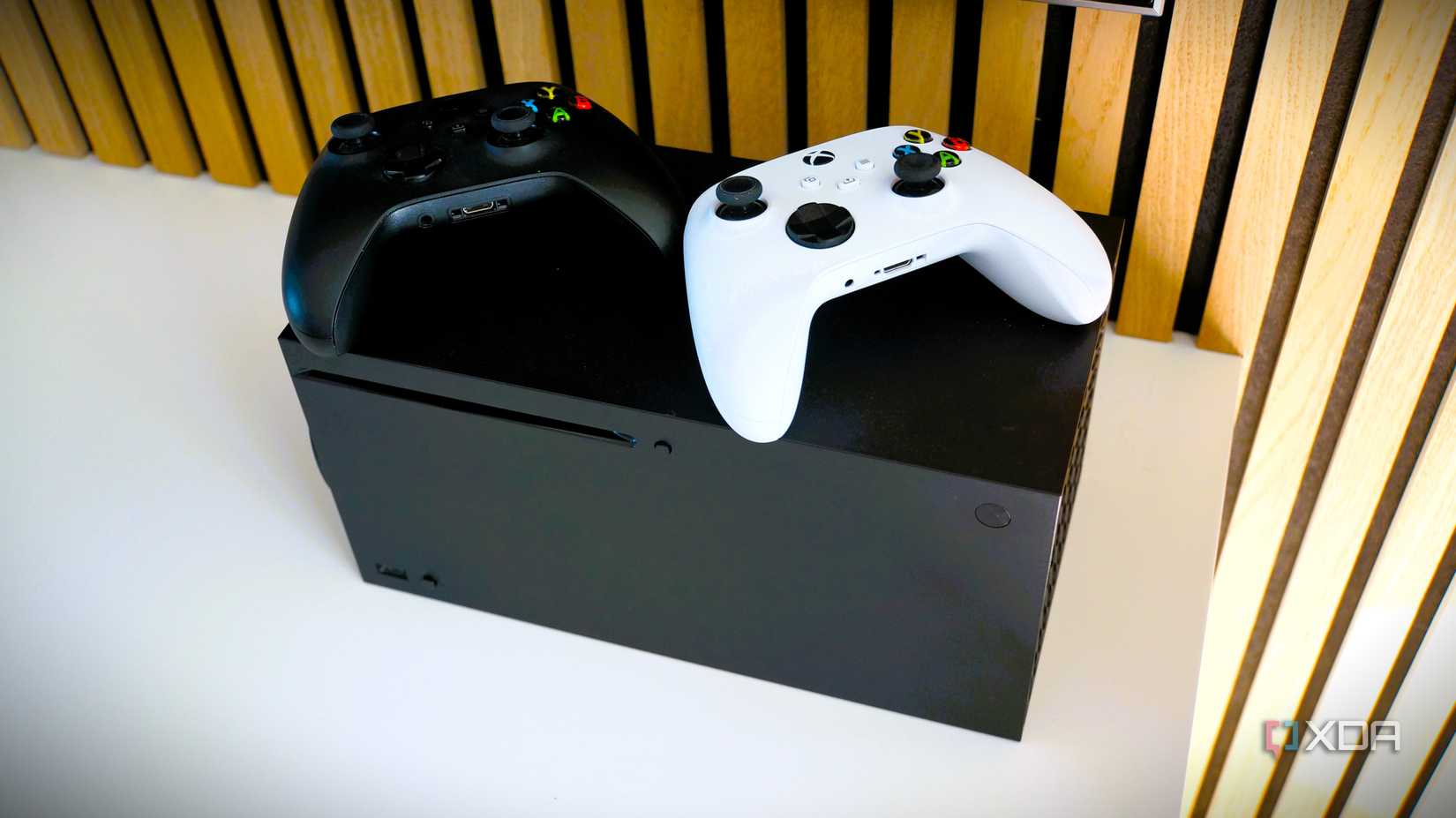 xbox series x with a black controller and a white controller on top of it