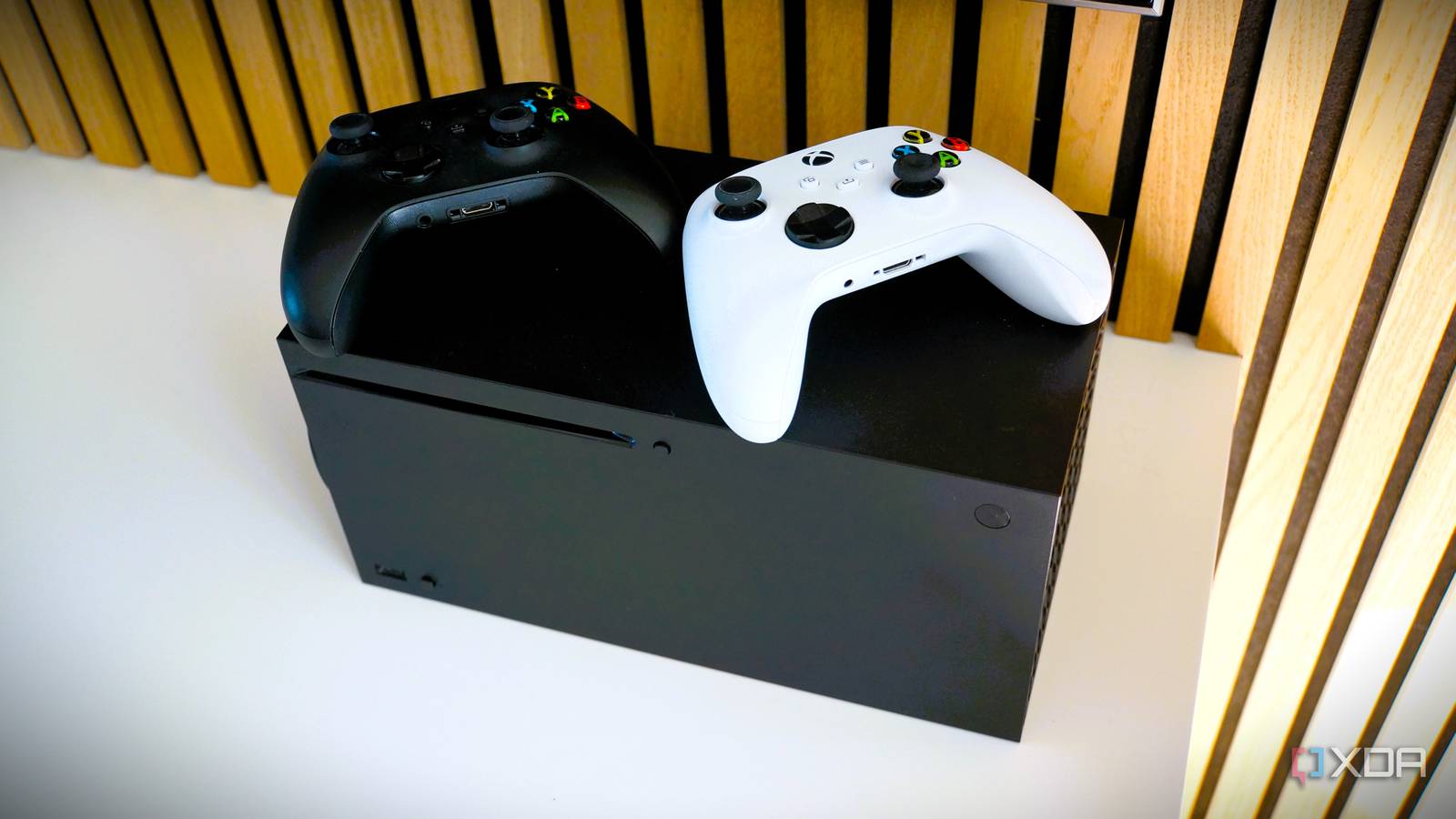 xbox series x with a black controller and a white controller on top of it