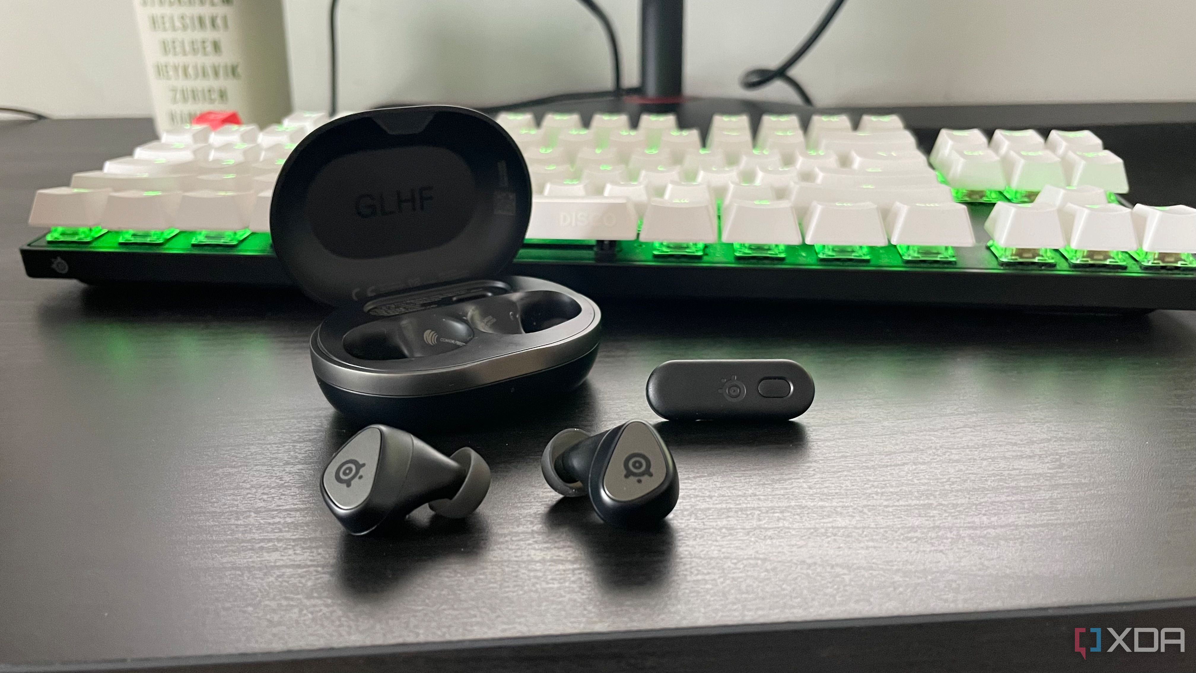 The SteelSeries Arctis GameBuds displayed outside their case in front of a mechanical gaming keyboard.