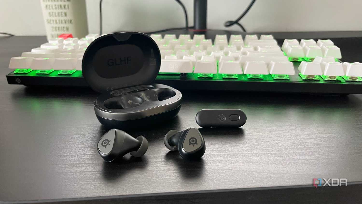 The SteelSeries Arctis GameBuds displayed outside their case in front of a mechanical gaming keyboard.