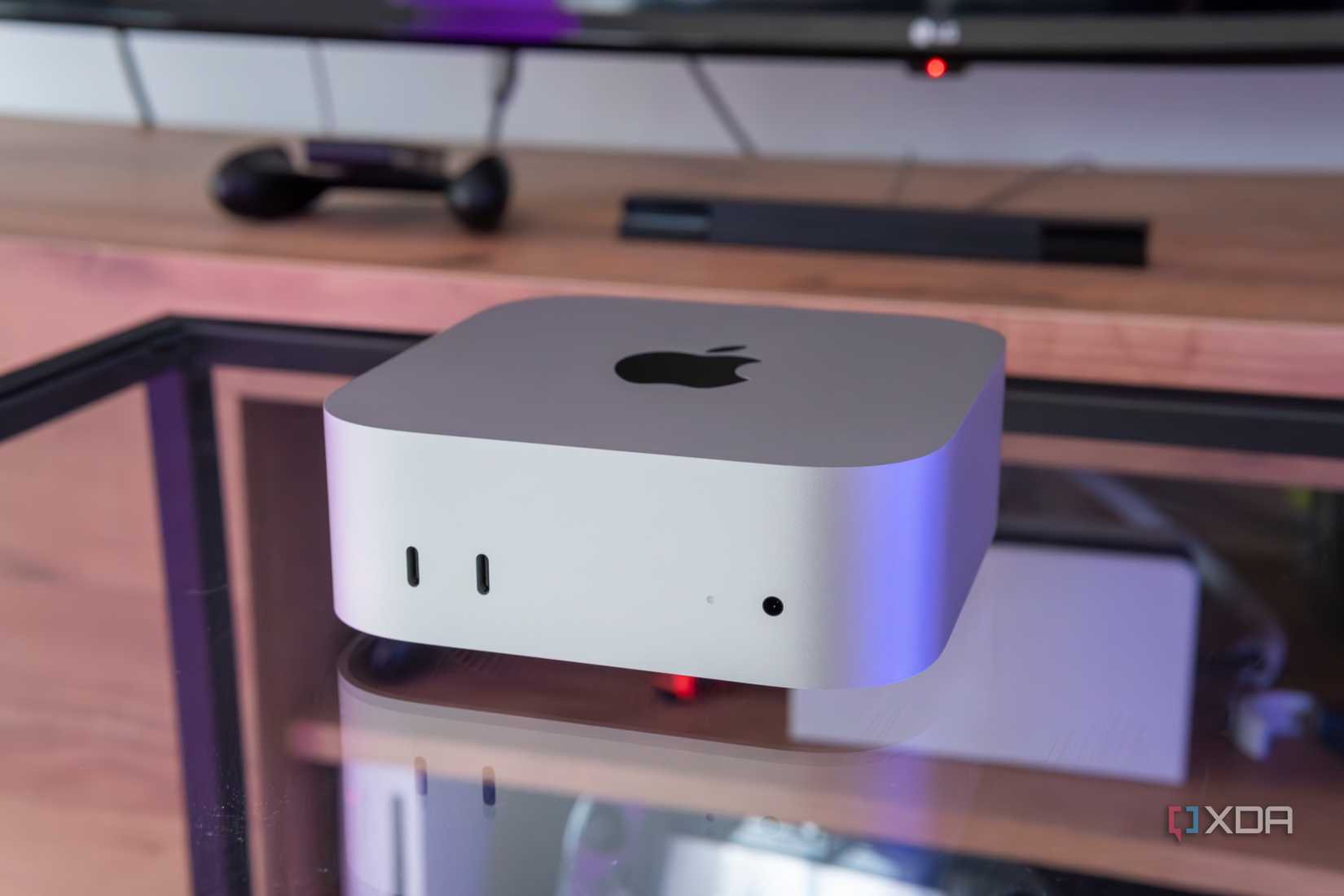 A Mac Mini M4 on a glass table with a TV stand in the background