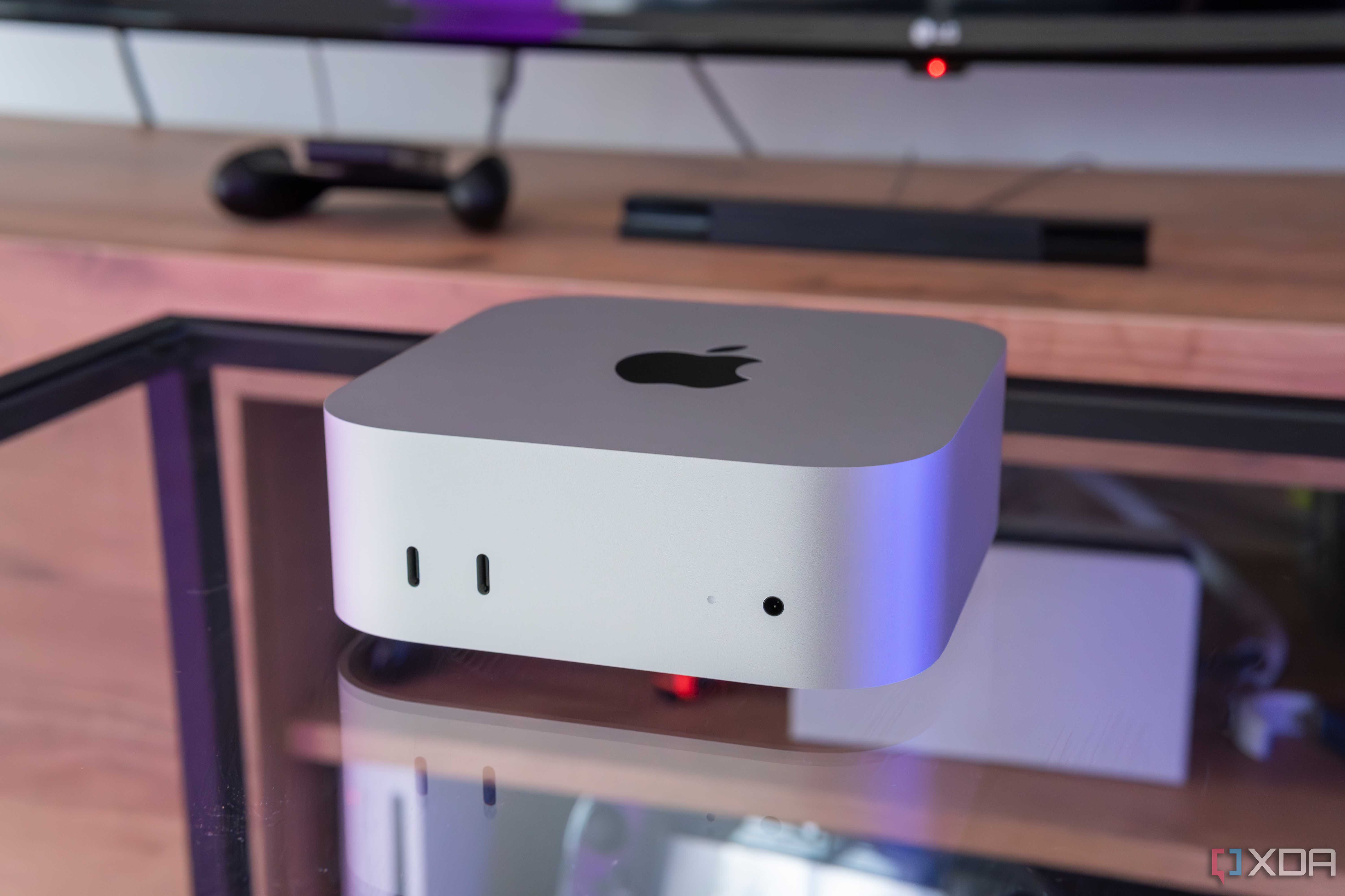 A Mac Mini M4 on a glass table with a TV stand in the background