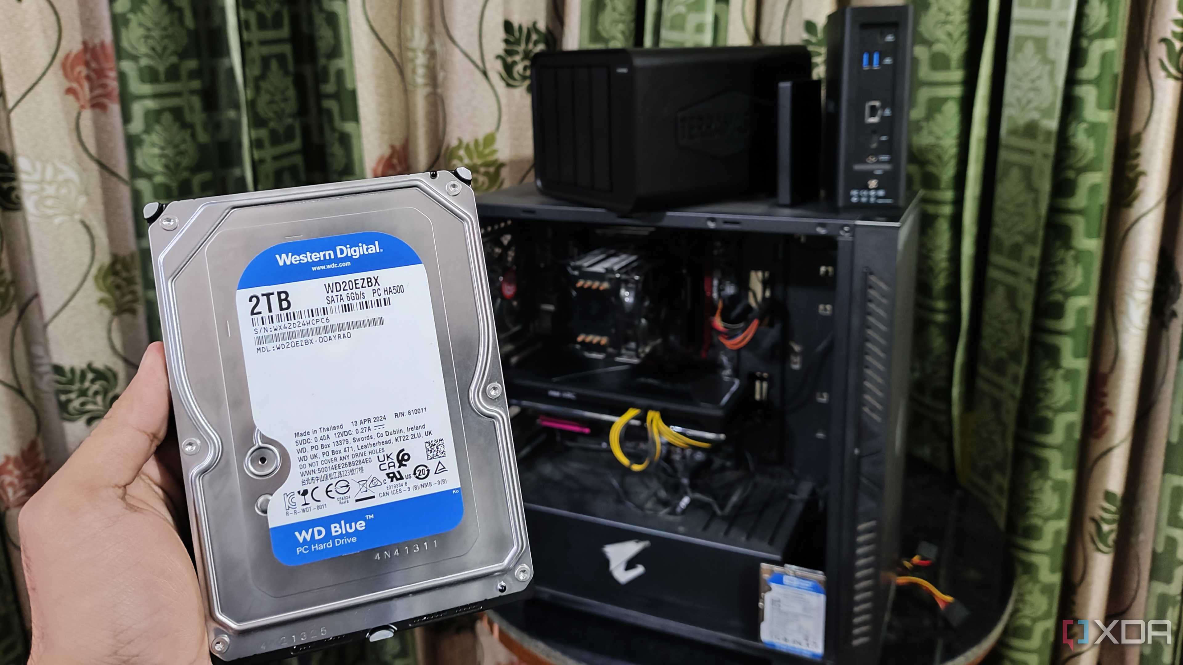A person holding an HDD in front of a PC and two TerraMaster NAS units