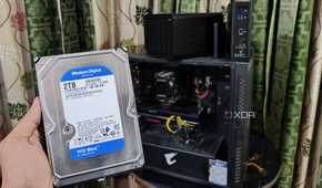A person holding an HDD in front of a PC and two TerraMaster NAS units