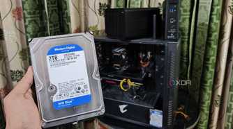 A person holding an HDD in front of a PC and two TerraMaster NAS units