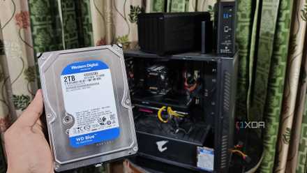 A person holding a hard drive in front of a PC and two TerraMaster NAS drives