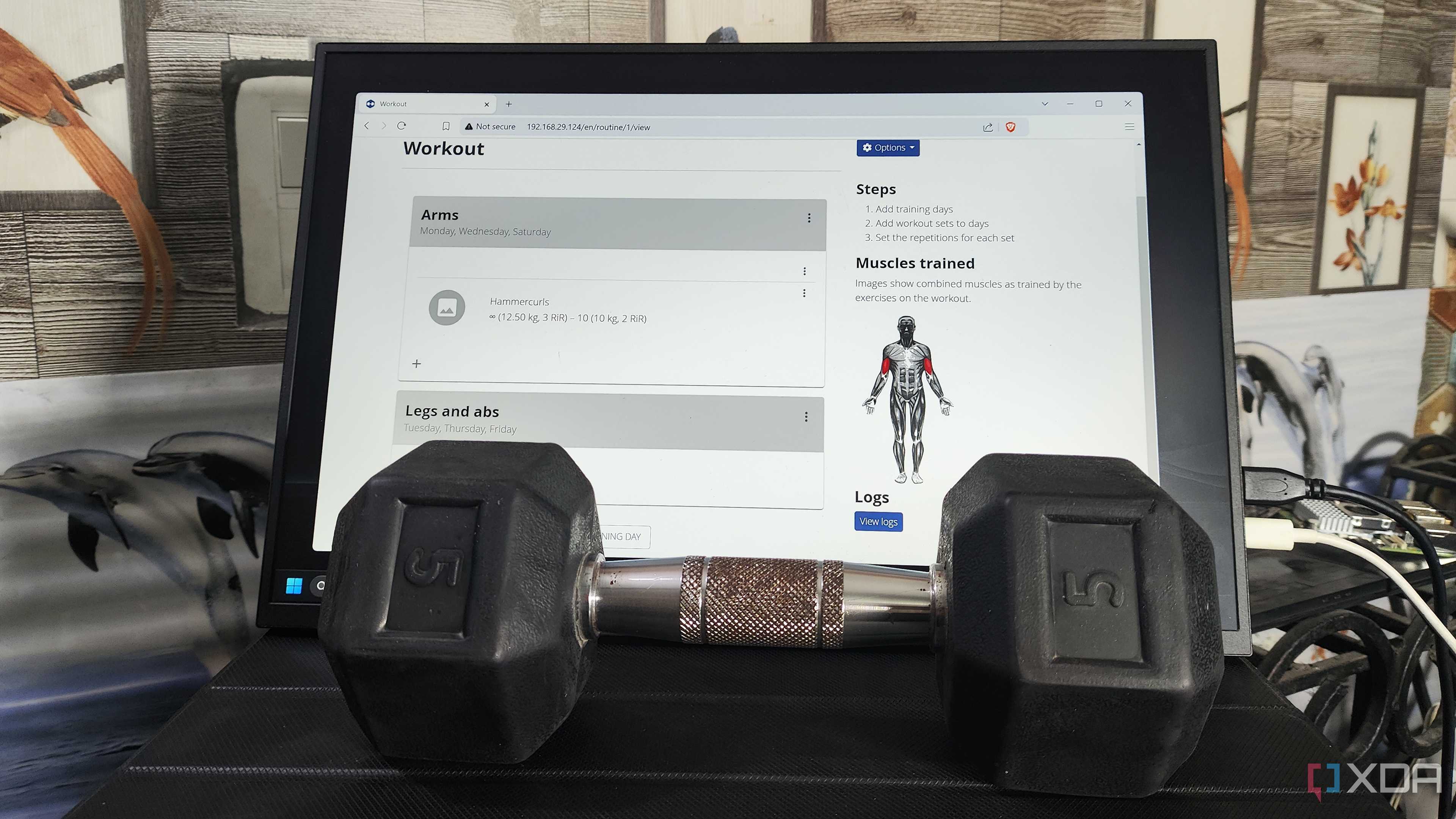 A dumbbell placed in front of a monitor displaying the wger UI