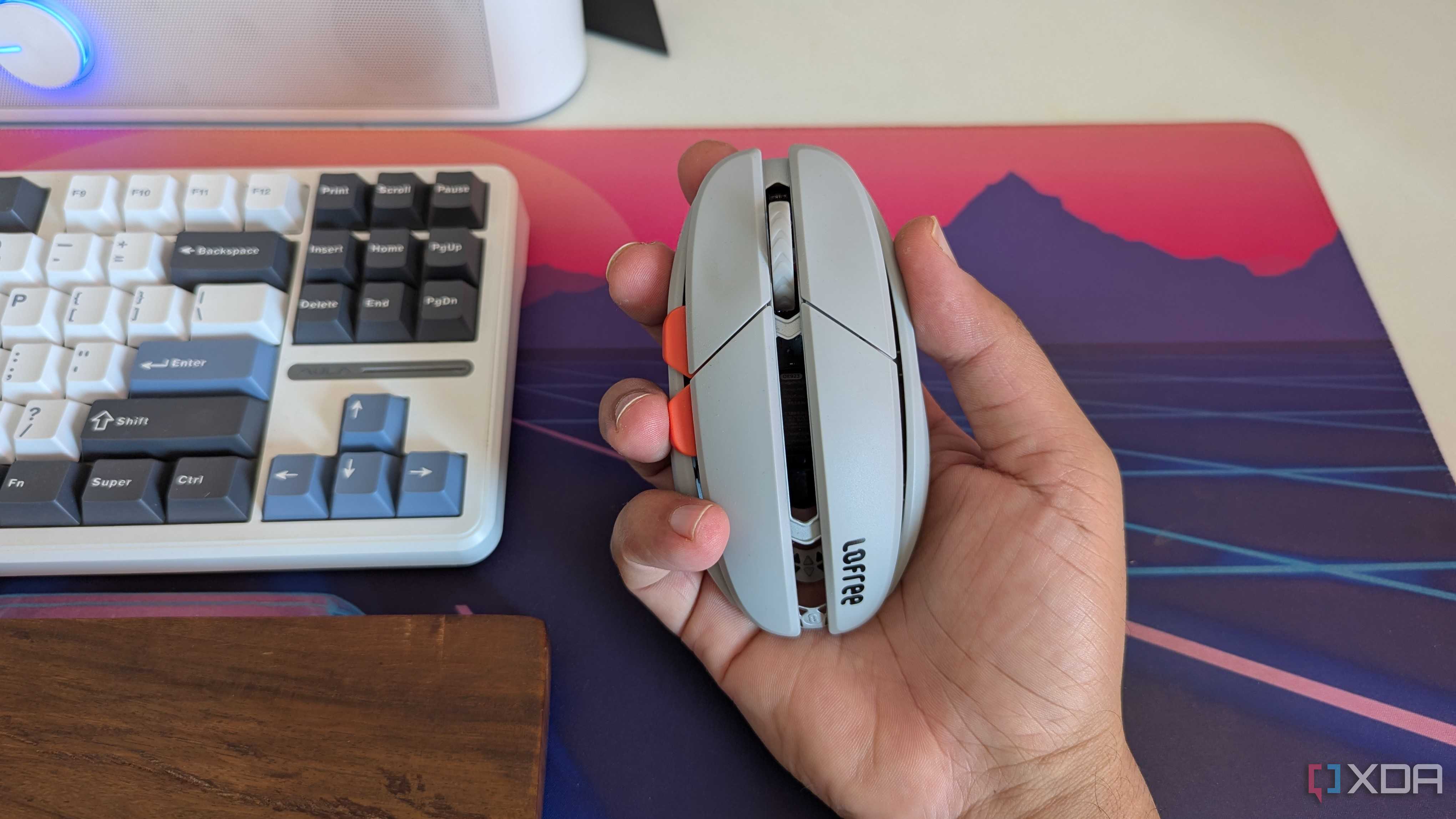 A grey gaming mouse in hand next to a keyboard and wrist rest