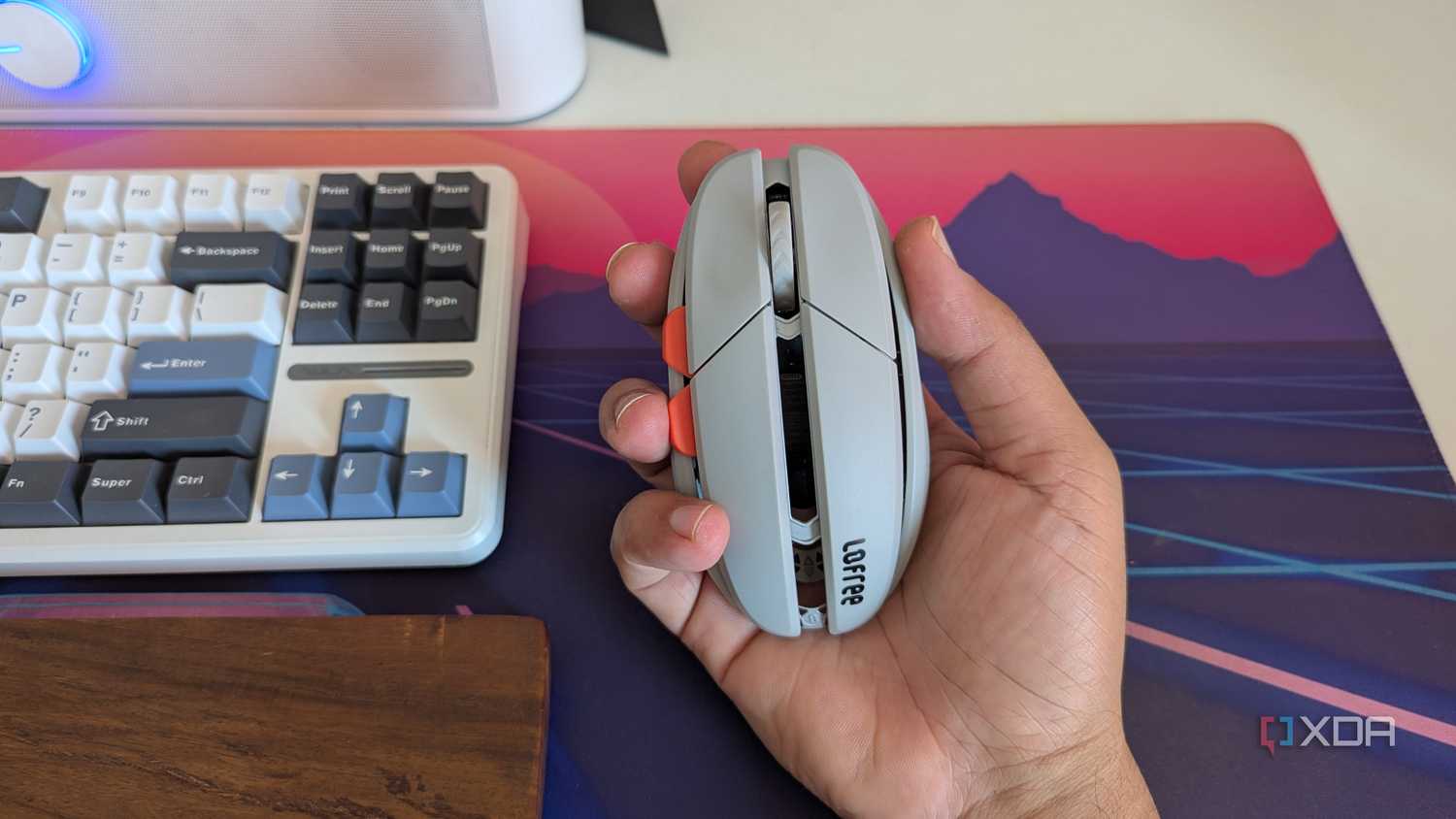 A grey gaming mouse in hand next to a keyboard and wrist rest