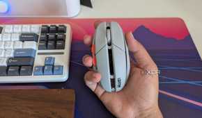 A grey gaming mouse in hand next to a keyboard and wrist rest