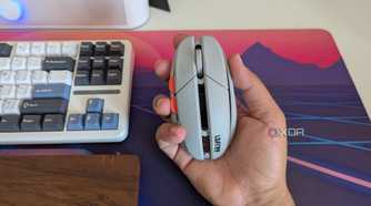 A grey gaming mouse in hand next to a keyboard and wrist rest