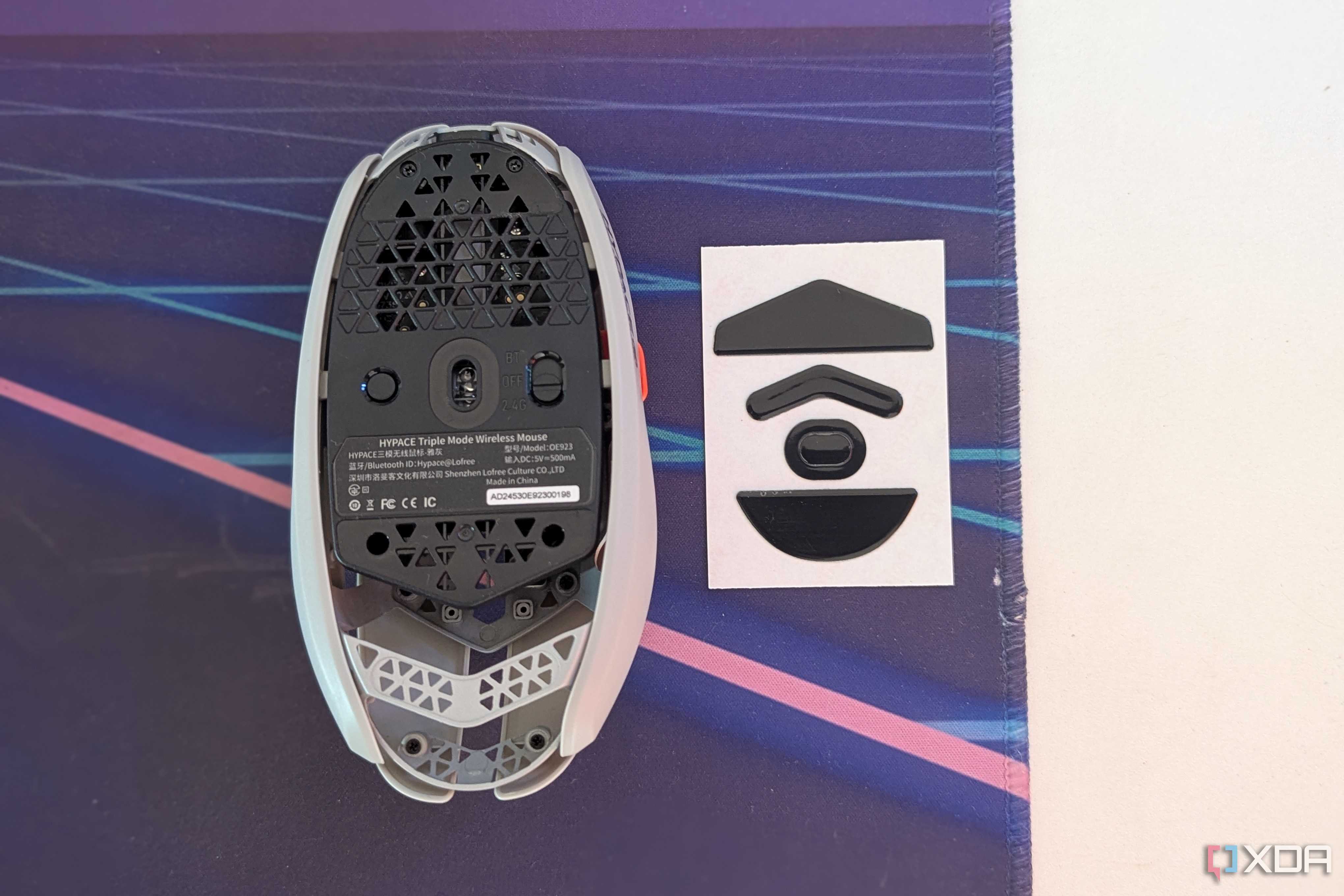 Bottom view of a gaming mouse next to mouse feet on a desk mat