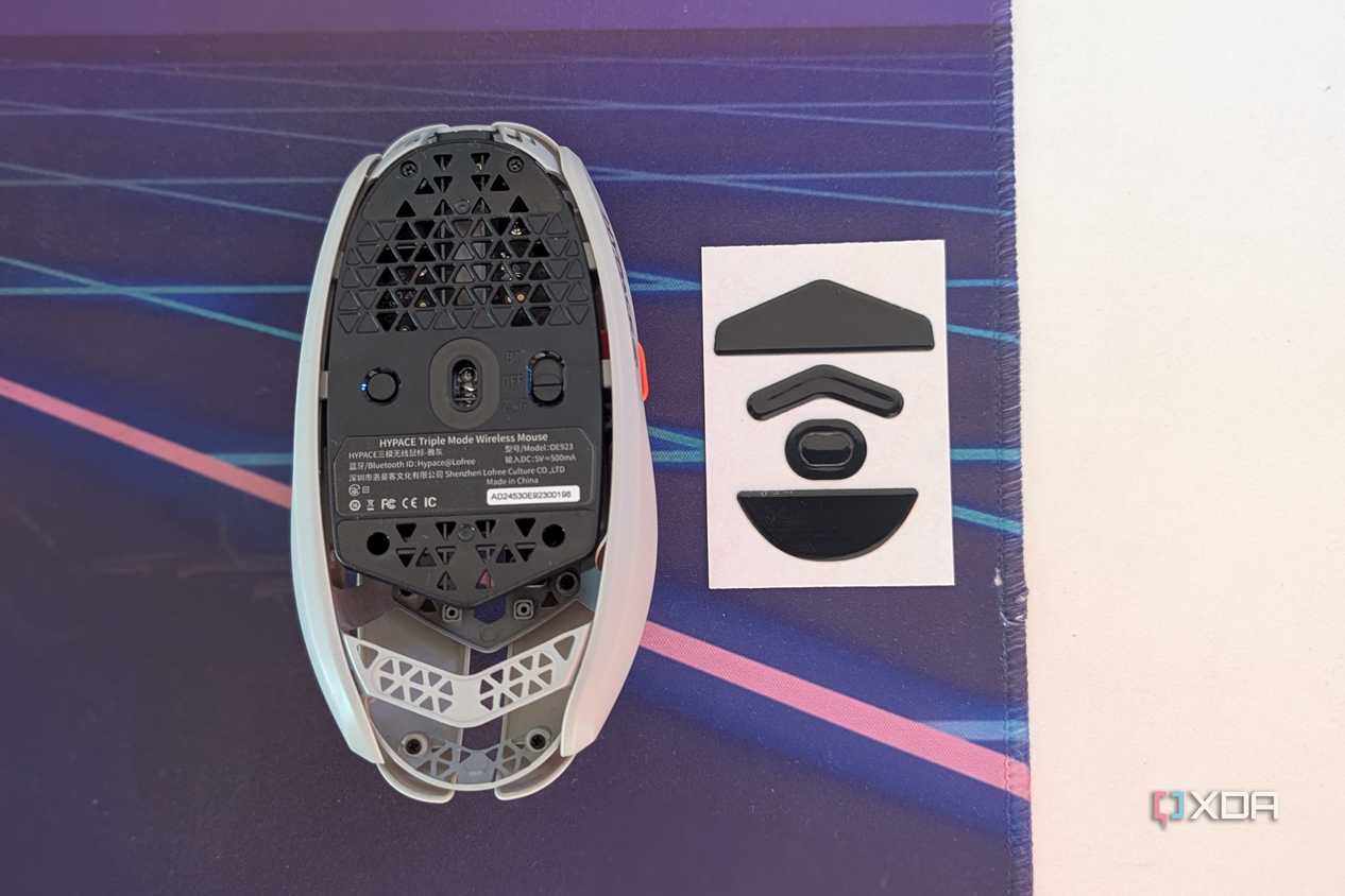 Bottom view of a gaming mouse next to mouse feet on a desk mat