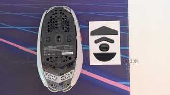 Bottom view of a gaming mouse next to mouse feet on a desk mat