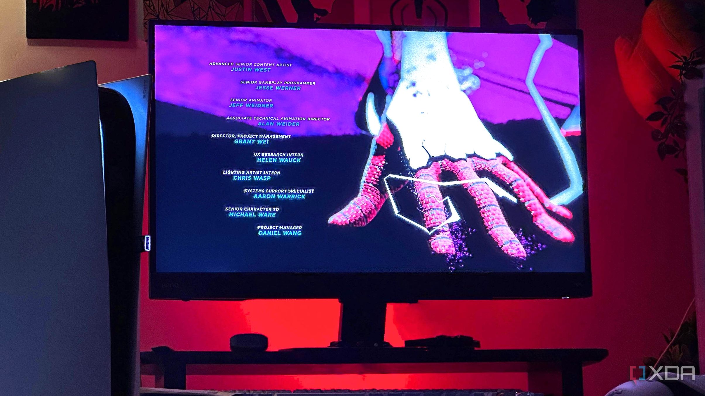 Una imagen de una consola PlayStation 5 junto a una pantalla de monitor con luces rojas de fondo.