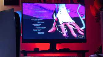 An image of a PlayStation 5 console sitting beside a monitor screen with red lights in the background.