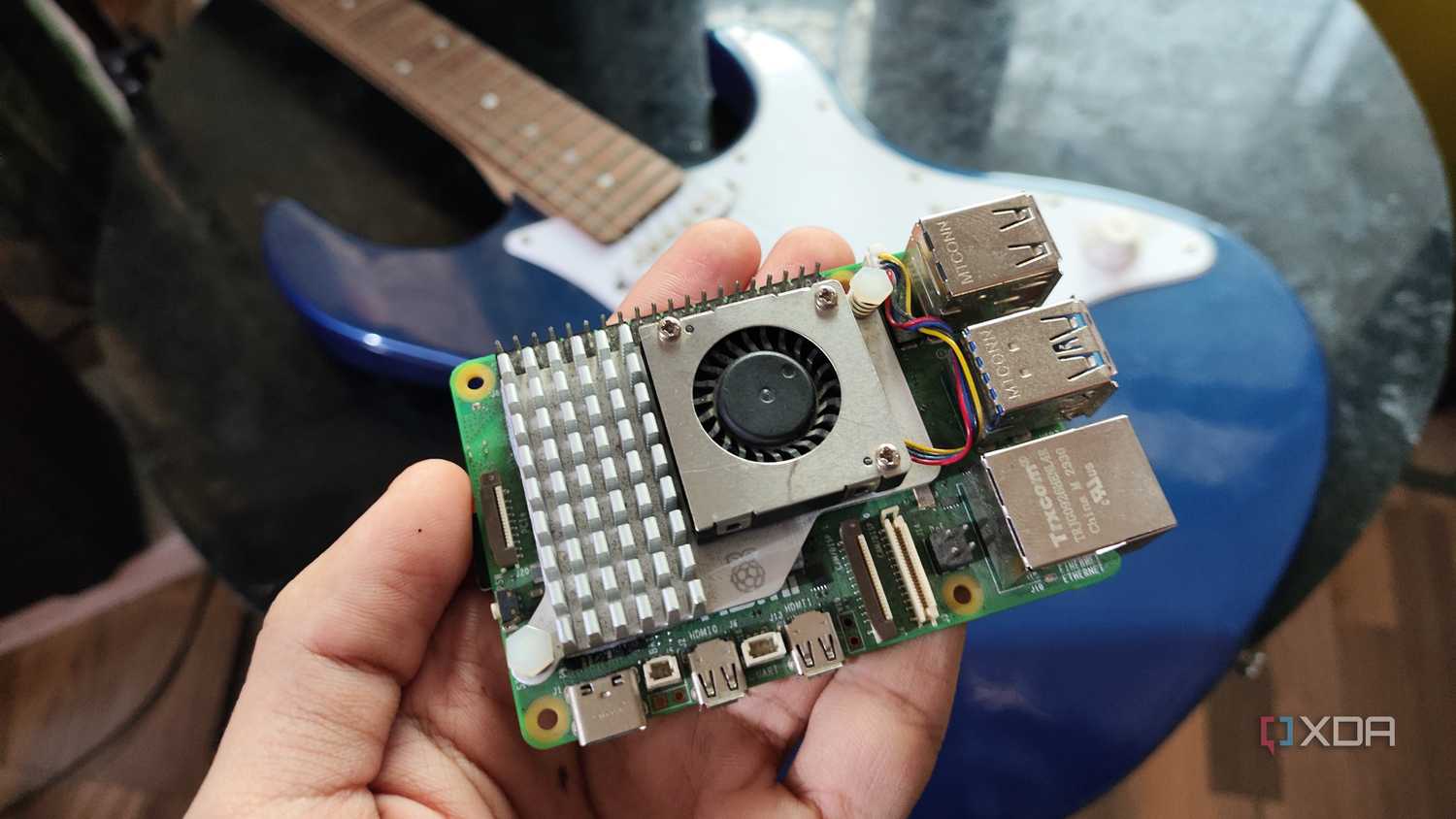A person holding a Raspberry Pi 5 in front of a Yamaha Pacifica 012