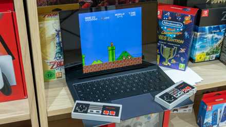 A Windows 11 laptop running Super Mario Bros on an emulator. Two wireless NES controllers rest on it.