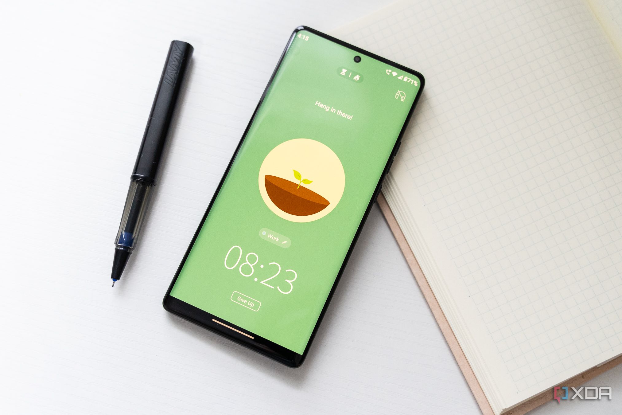  A picture of a smartphone displaying a growing tree in the Forest pomodoro app. The phone is next to a pen and notebook. 