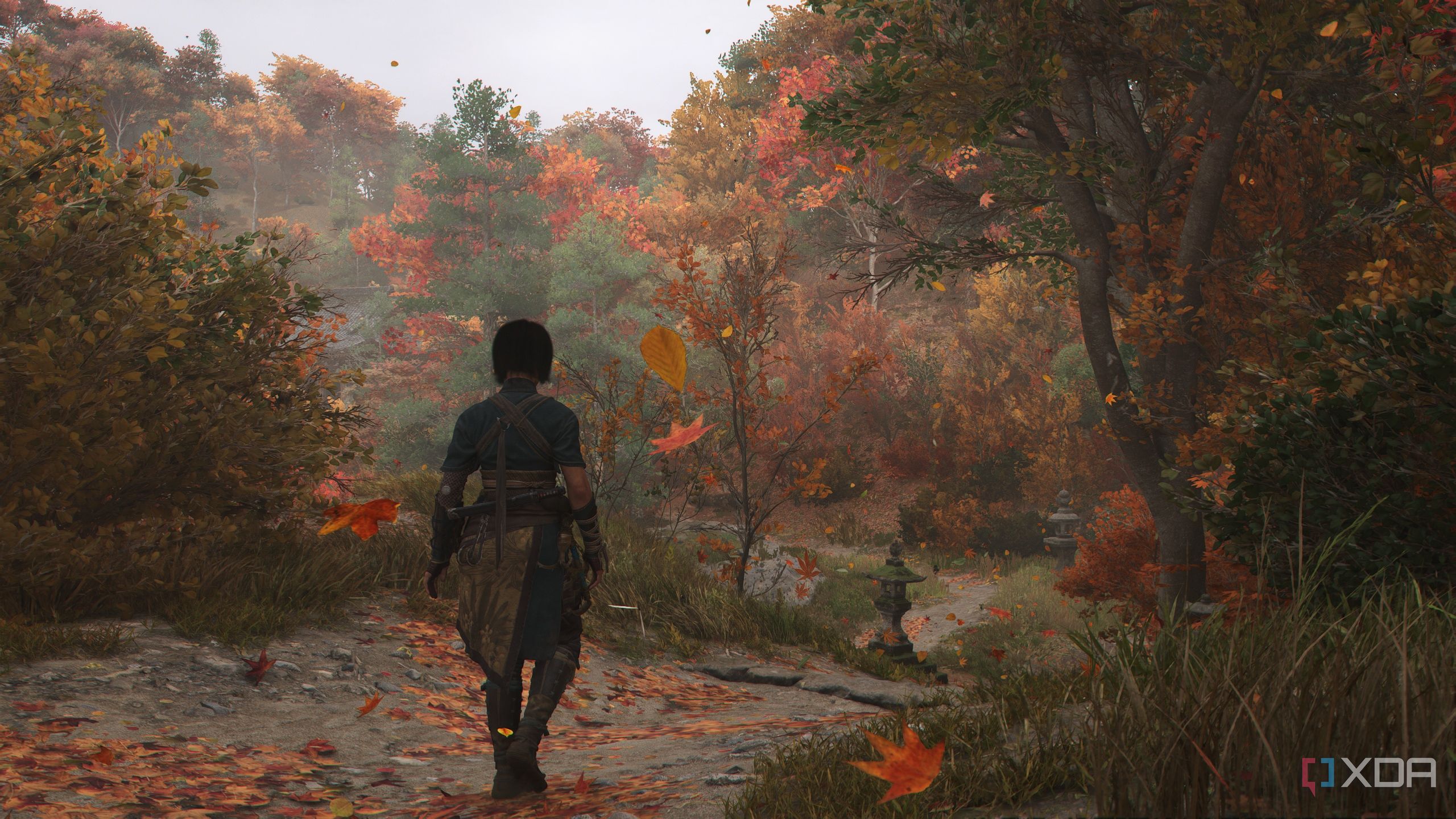 A screenshot from Assassin's Creed Shadows, showing Naoe, the female protagonist, walking through a beautiful mountain trail with autumn leaves falling around her.