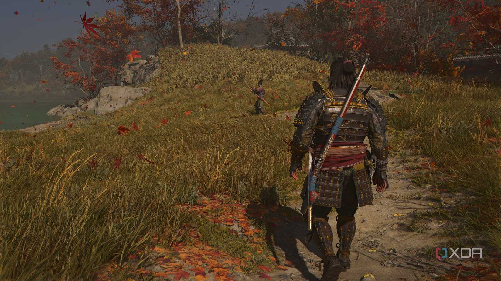 A screenshot from Assassin's Creed Shadows, showing Yasuke, the Samurai, walk up to another man with a sword in a grassy and windy field.