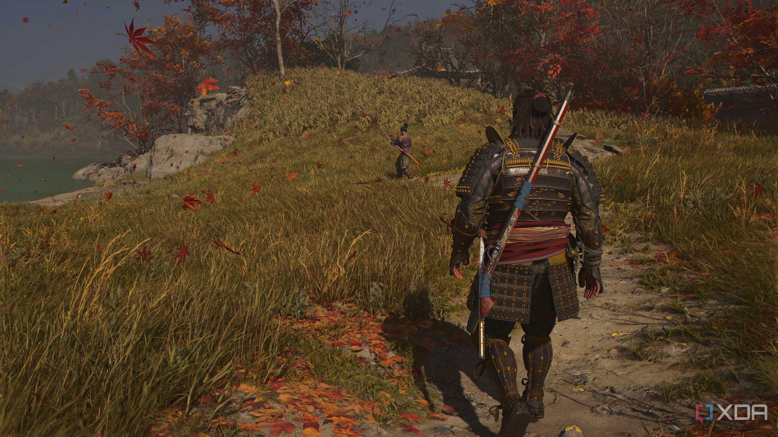 A screenshot from Assassin's Creed Shadows, showing Yasuke, the Samurai, walk up to another man with a sword in a grassy and windy field.