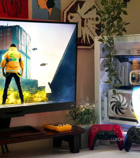 An image showing a PC setup with Cyberpunk 2077 on the monitor, and two gaming controllers resting against the PC case.