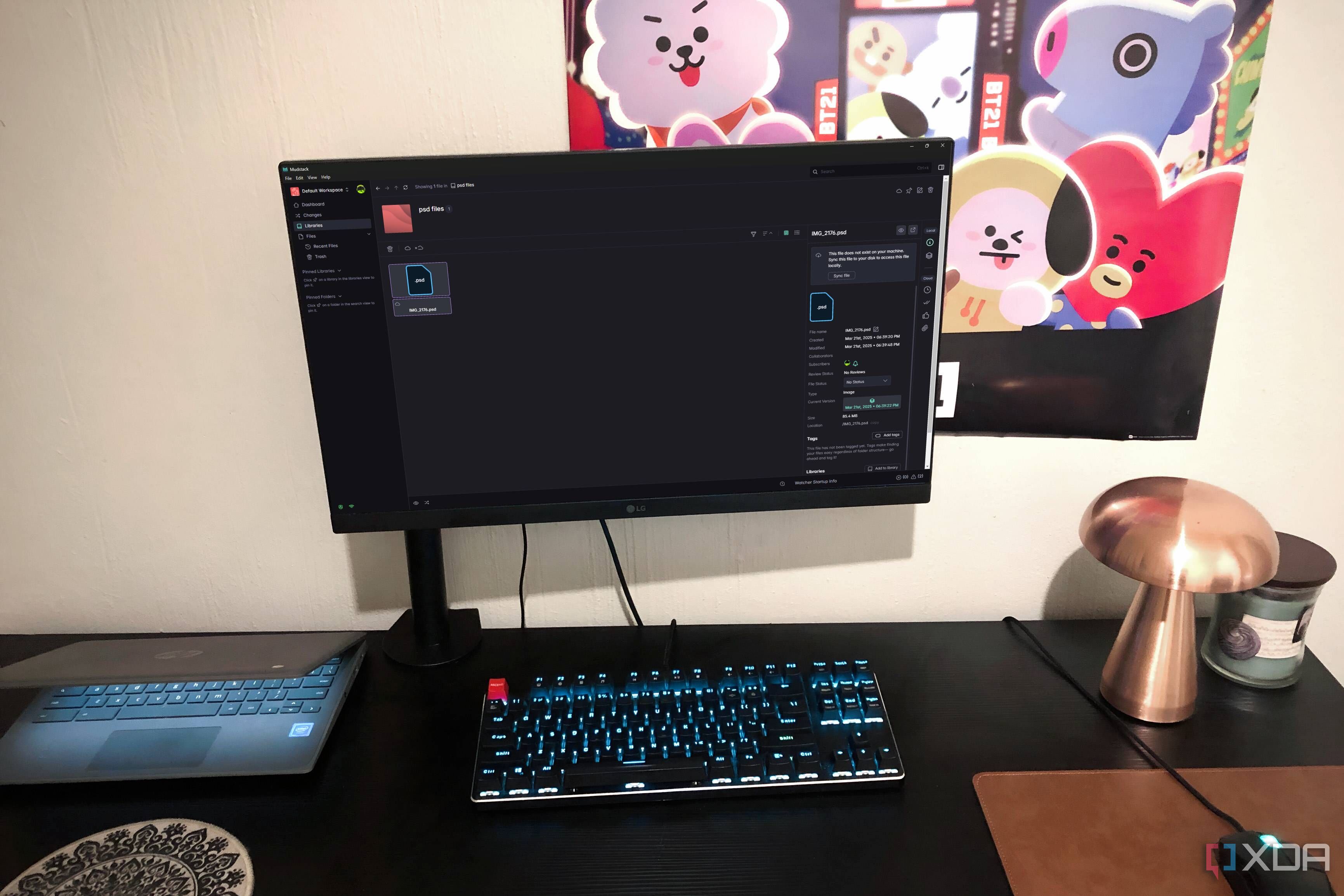 Herramienta de almacenamiento en la nube Mudstack mostrada en una PC de escritorio, con una lámpara, un Chromebook y un póster a la vista