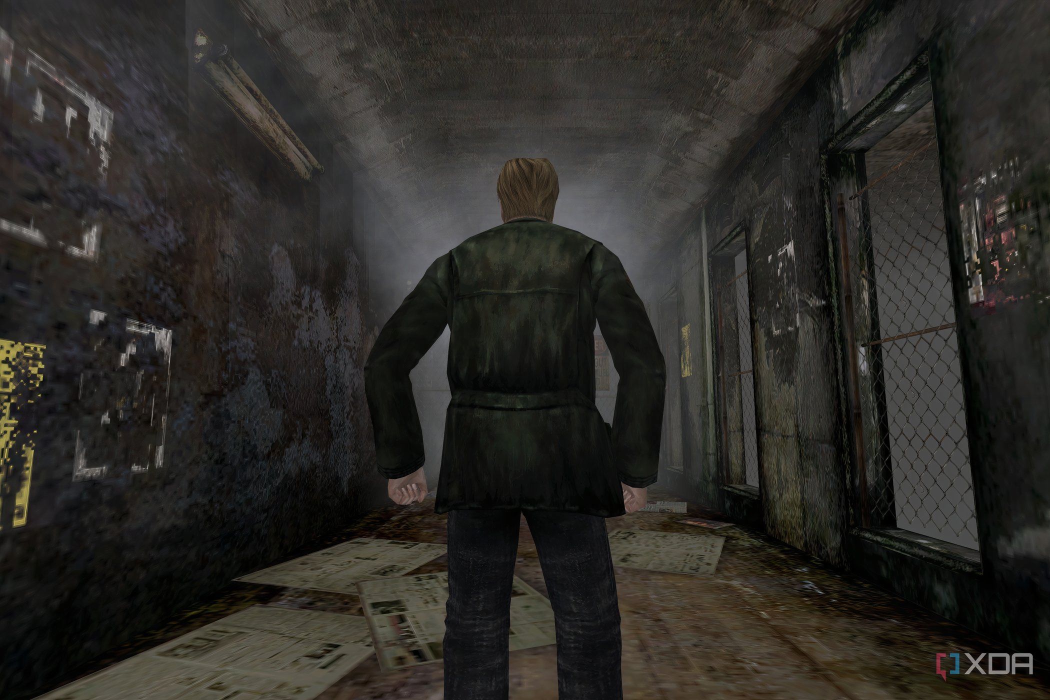 An in-game screenshot from the game Silent Hill 2, showing a man standing in the middle of a dingy alley.