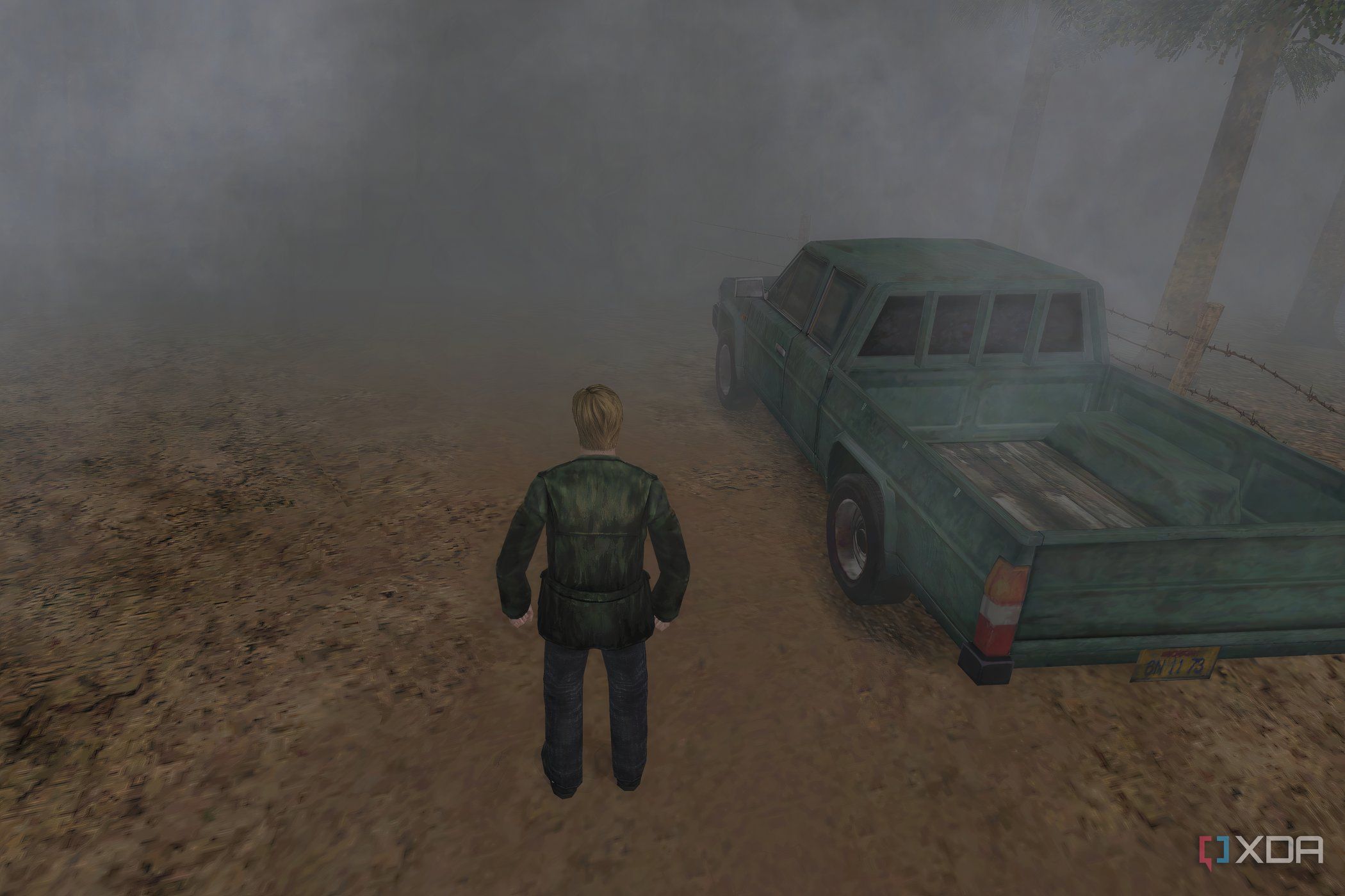 An in-game screenshot from the game Silent Hill 2, showing a man standing next to a green pickup truck while standing on a dirt road.