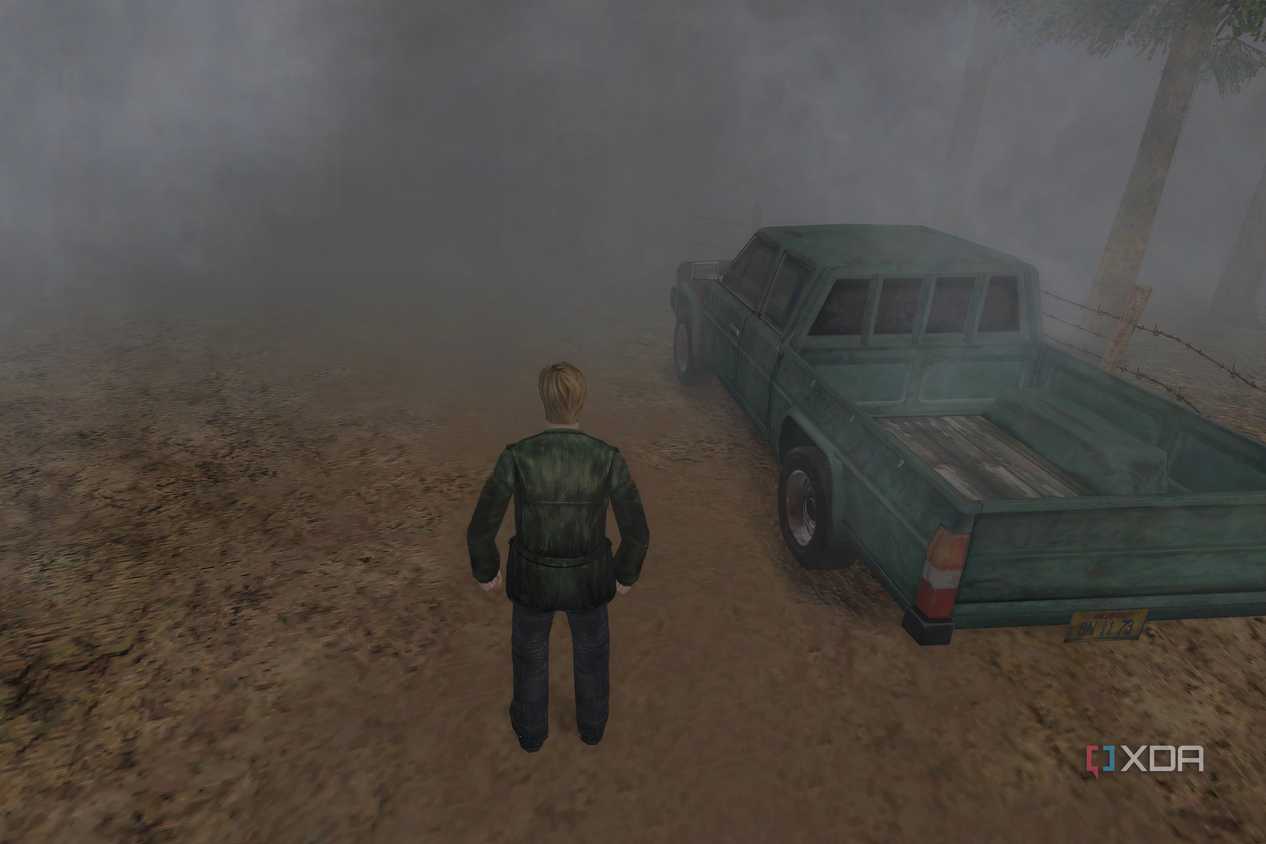 An in-game screenshot from the game Silent Hill 2, showing a man standing next to a green pickup truck while standing on a dirt road.