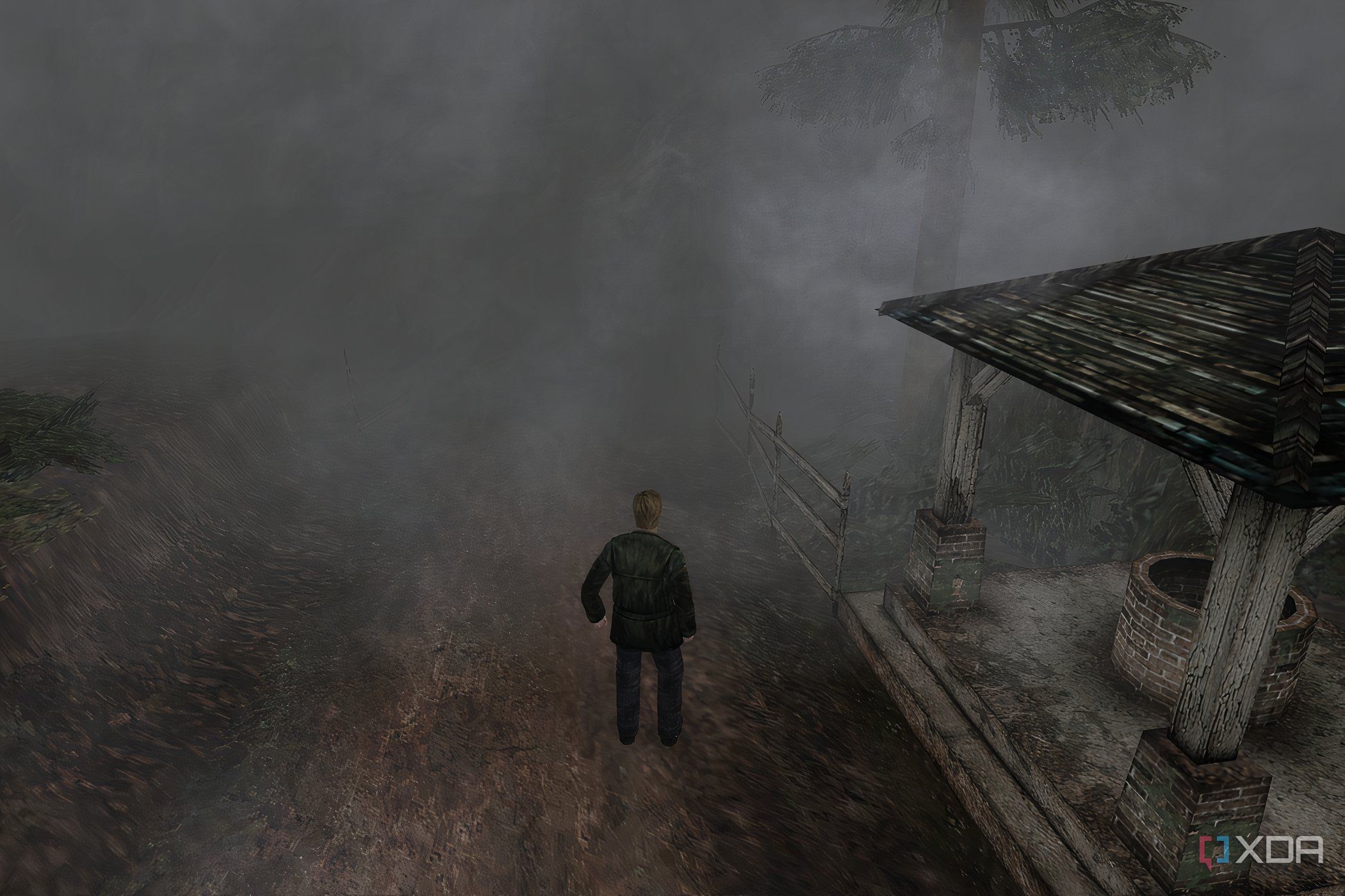 An in-game screenshot from the game Silent Hill 2, showing a man standing next to a dilapidated gazebo while surrounded by thick fog.