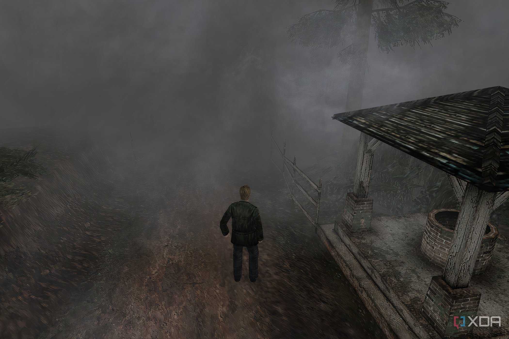 An in-game screenshot from the game Silent Hill 2, showing a man standing next to a dilapidated gazebo while surrounded by thick fog.