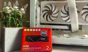 An image of a red box holding a 2TB SSD from XPG, resting against a faux flower pot and an unlit PC case