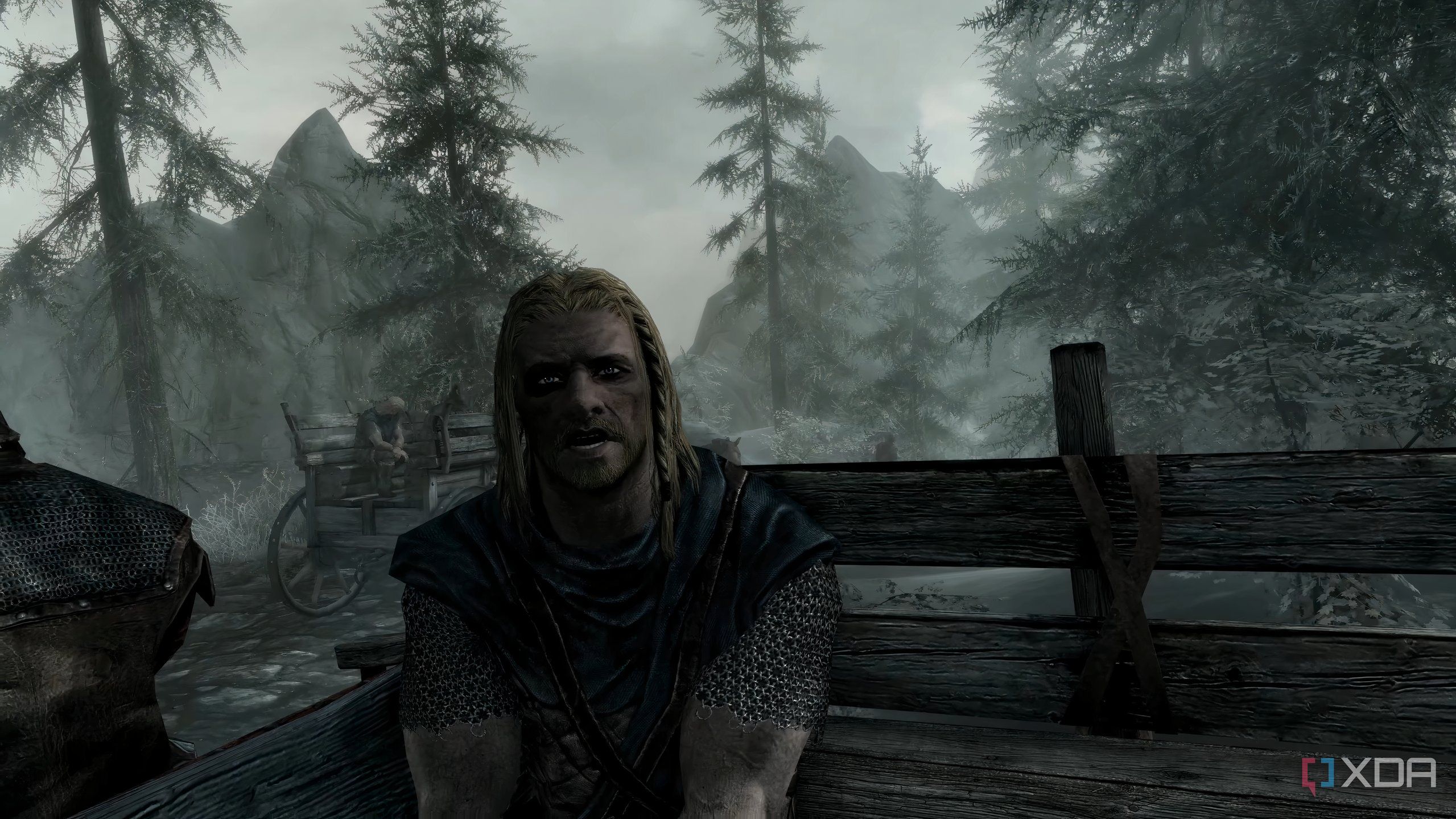 A screenshot from the game "The Elder Scrolls V: Skyrim", showing Ralof address the player while both sit in the back of an open wooden cart.