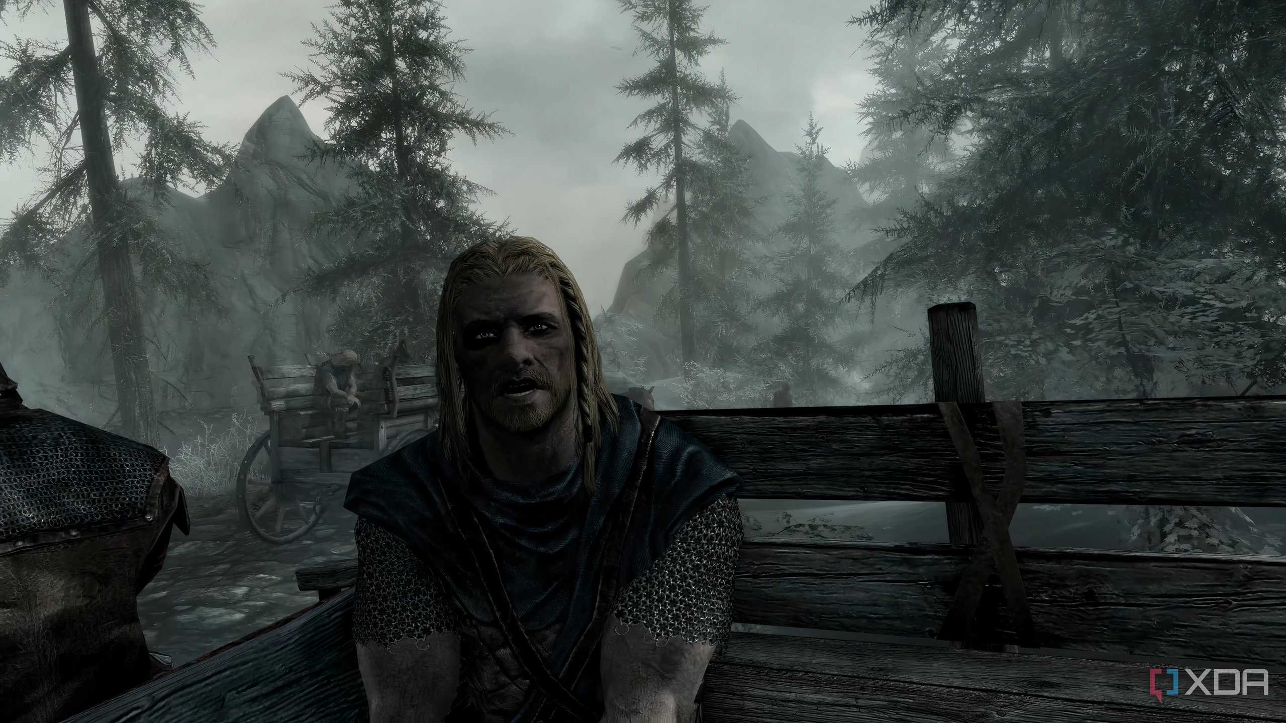A screenshot from the game "The Elder Scrolls V: Skyrim", showing Ralof address the player while both sit in the back of an open wooden cart.