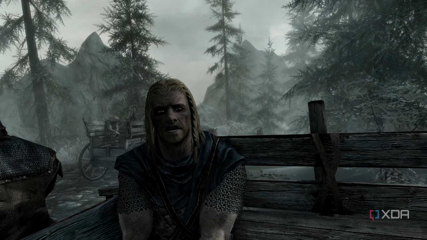 A screenshot from the game "The Elder Scrolls V: Skyrim", showing Ralof address the player while both sit in the back of an open wooden cart.