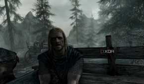 A screenshot from the game "The Elder Scrolls V: Skyrim", showing Ralof address the player while both sit in the back of an open wooden cart.