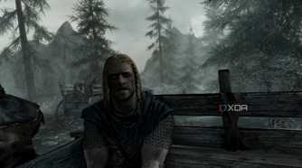 A screenshot from the game "The Elder Scrolls V: Skyrim", showing Ralof address the player while both sit in the back of an open wooden cart.