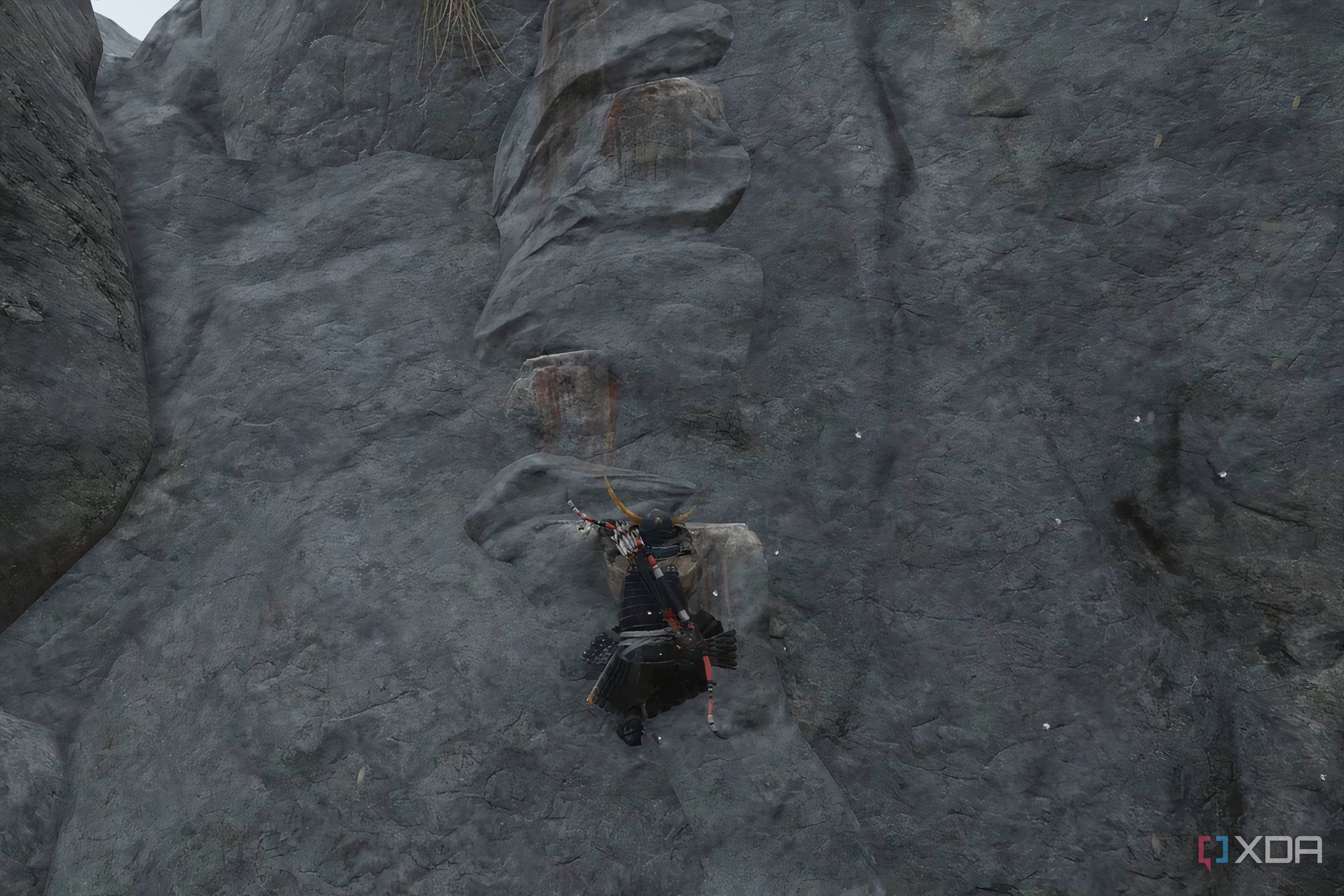 A screenshot from Ghost of Tsushima, showing Jin Sakai climbing up a cliff face with white-painted handholds.