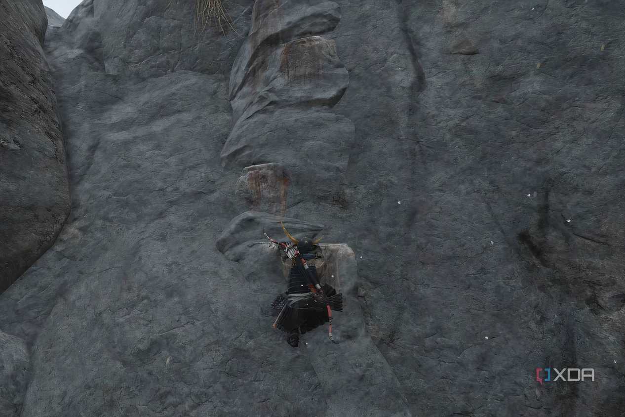 A screenshot from Ghost of Tsushima, showing Jin Sakai climbing up a cliff face with white-painted handholds.
