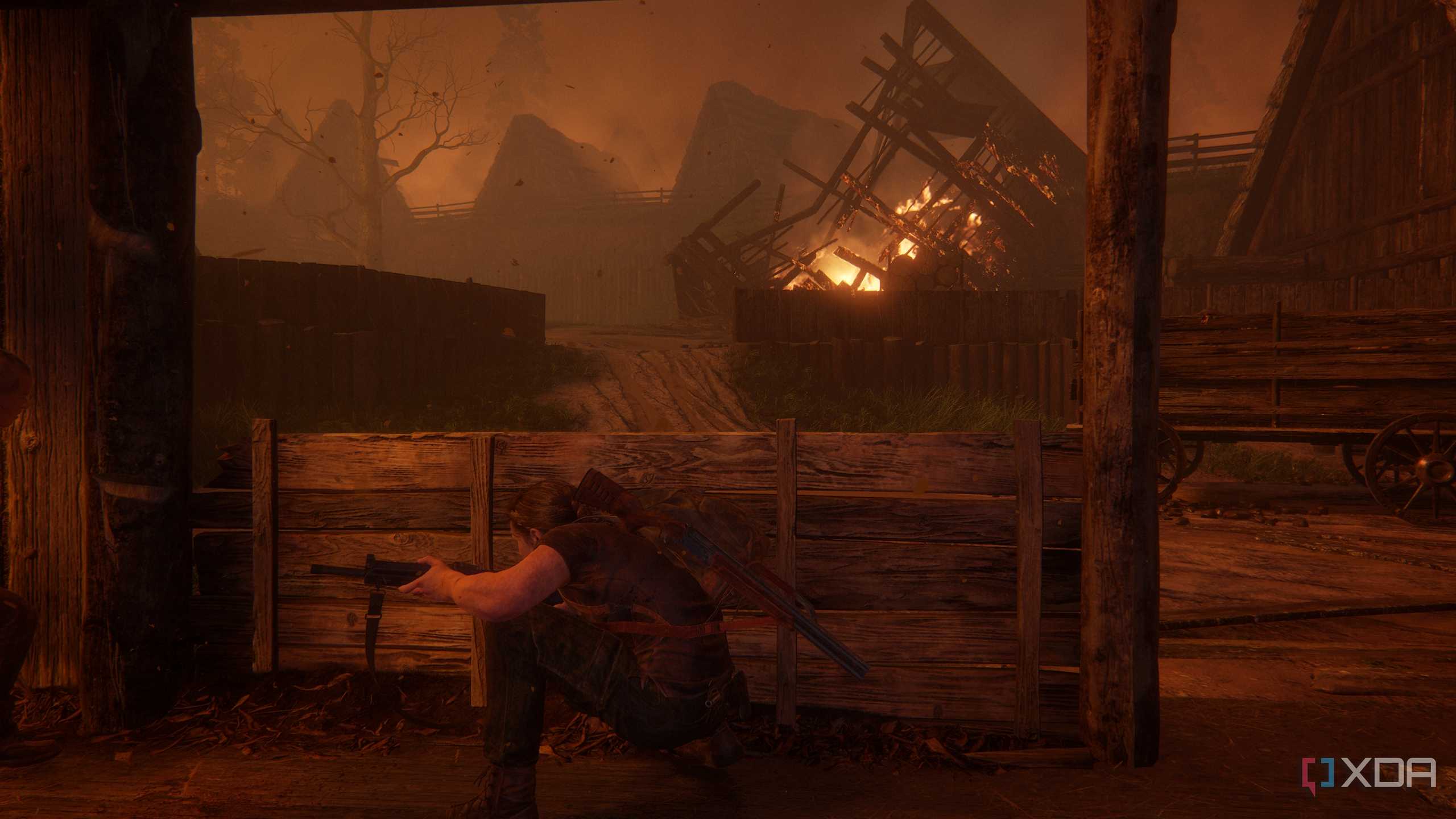 A screenshot from the game The Last of Us Part II, showing Abby taking cover in a fiery wooden village.
