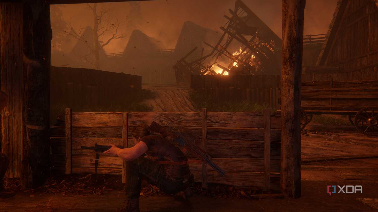 A screenshot from the game The Last of Us Part II, showing Abby taking cover in a fiery wooden village.
