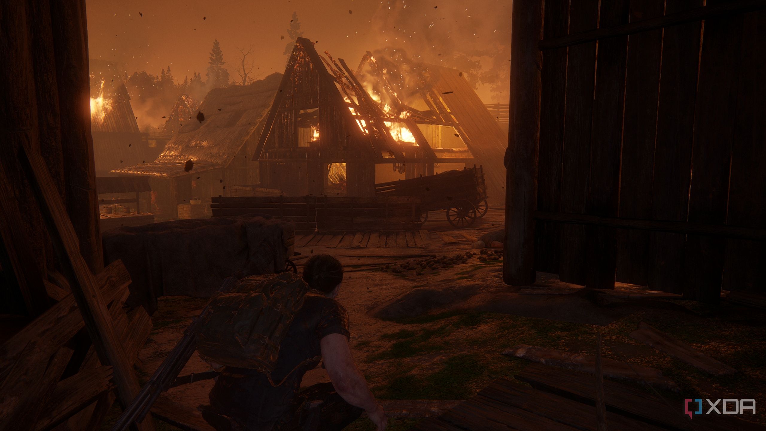 A screenshot from the game The Last of Us Part II, showing Abby crouching while a village burns.