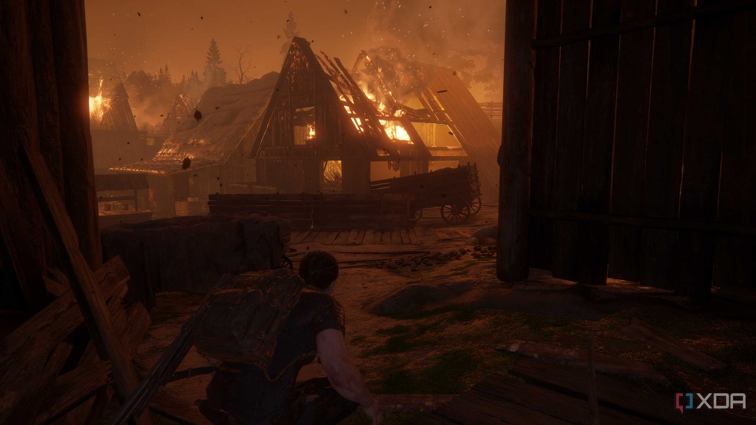 A screenshot from the game The Last of Us Part II, showing Abby crouching while a village burns.