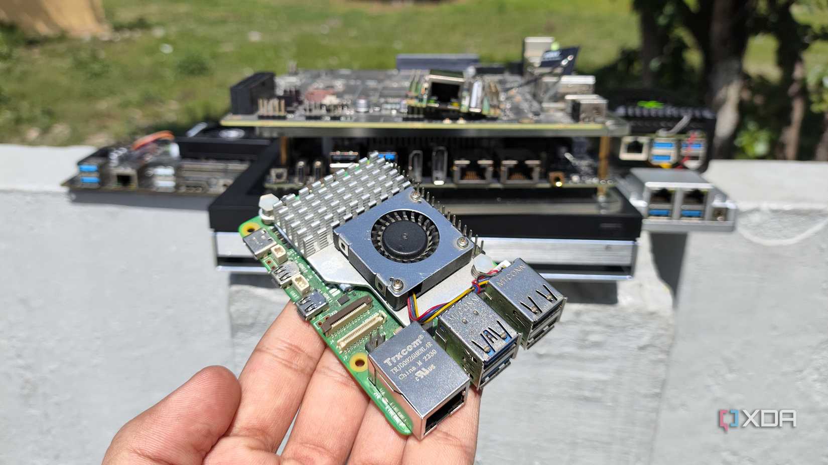 A person holding a Raspberry Pi in front of other SBCs, mini PCs and NAS